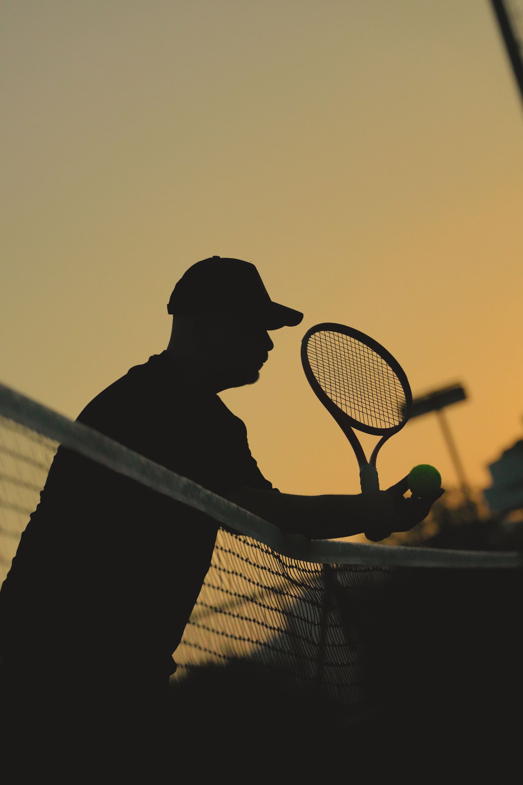 Silhouette of a player serving against a warm evening sky